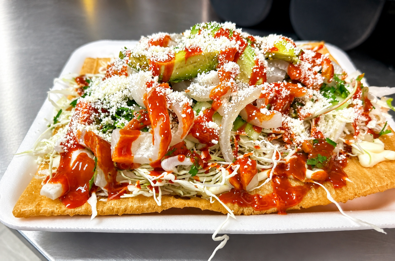 Loaded chicharrón topped with cabbage, avocado, onion, queso fresco, and hot sauce