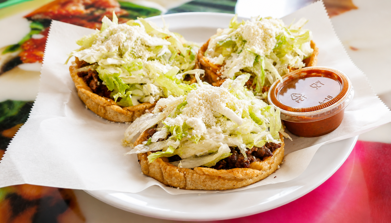 Three meat sopes topped with lettuce, crema, and queso fresco with salsa